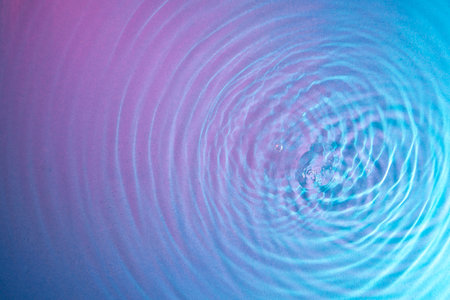 Top view of water droplet waves expanding on the water surface illuminated with blue and magenta lightの写真素材