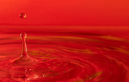 Background of Water drops splashing on the water surface forming waves illuminated with red lightの写真素材