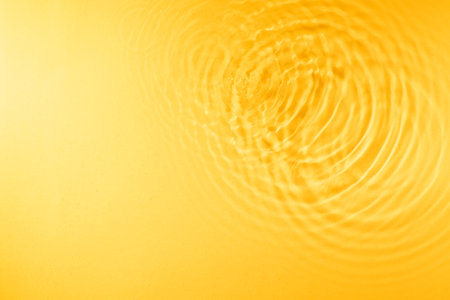 Background of water droplet waves expanding on the water surface illuminated with yellow lightの写真素材