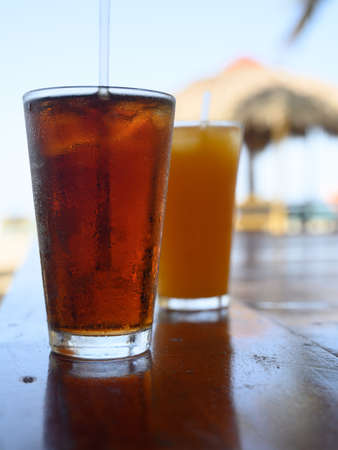 The photo shows Cola refreshments and passion fruit juice. Photo taken in bar on a Caribbean island. The beach and ocean line are visible in the background.Refreshments are visible in foreground.の写真素材