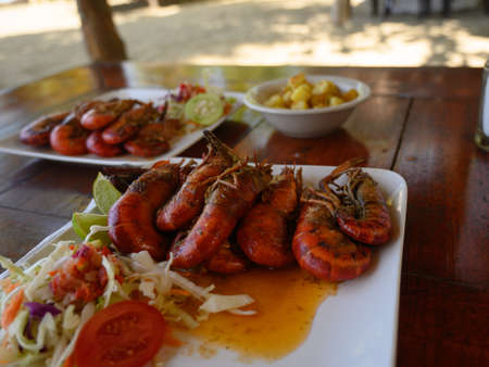 The photo shows two giant shrimp dishes with sauce. Also on a white glossy plate is a cabbage salad and a tomato. Dishes with hot food are arranged in a diamond shape.の写真素材