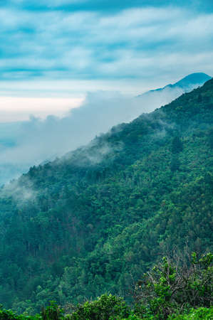 The photo shows mountains with green rainforests. Fog or steam is visible between the mountains. The...