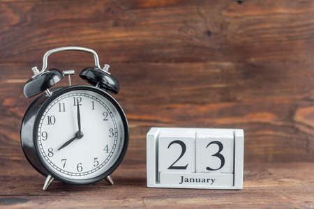 January 23 on a white calendar, next to a retro alarm clock on a dark wooden background. Calendar...