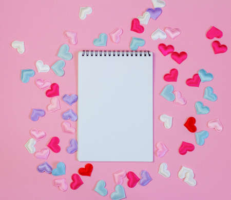 An open blank notebook on a pink background with hearts