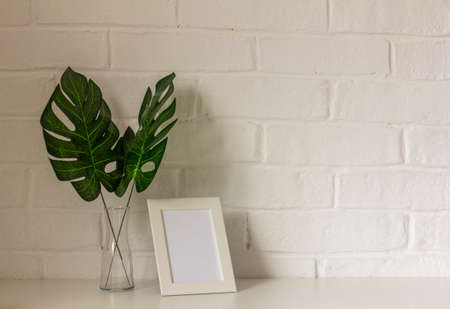 A home workplace.An empty picture frame or photo and monstera leaves in a vase are on the table....