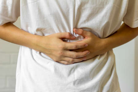The young man holds his stomach with his hands, experiencing pain and spasmsの写真素材