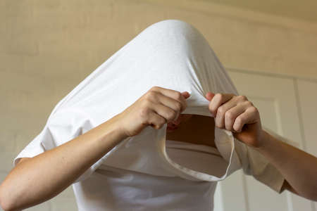 The young man pulls his T-shirt over his head, undresses