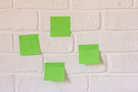 There are several green sticky notes hanging on the white brick wallの写真素材