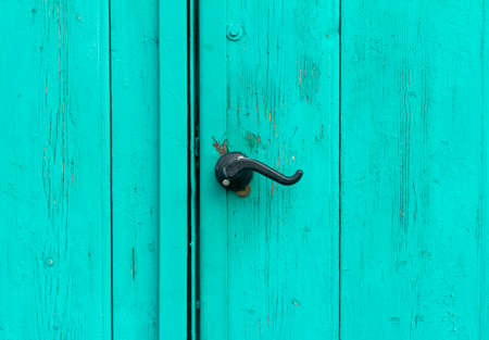 A fragment of an old wooden door of blue or turquoise color with a curly handleの写真素材