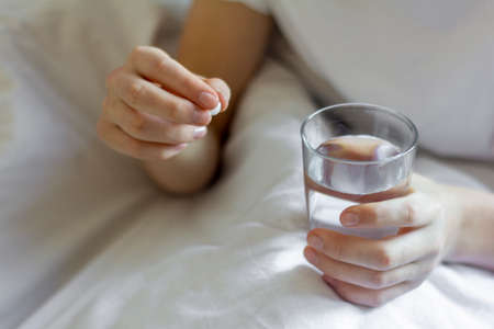 A sick young man is holding a pill and a glass of water.Taking medicationsの写真素材