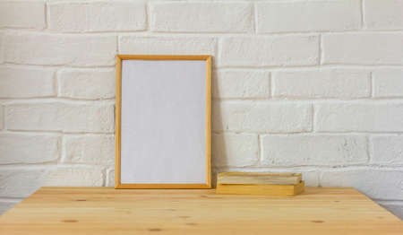 The layout of an empty photo frame and old books on a wooden tableの写真素材