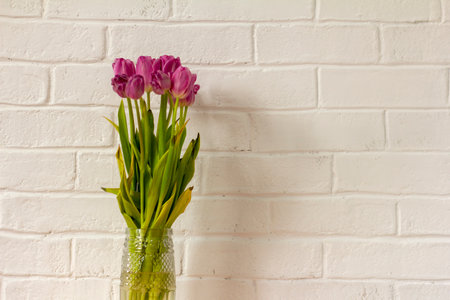 A fading bouquet of tulips in a vase on the tableの写真素材