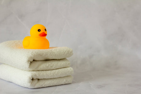 A yellow rubber duck for bathing on a stack of clean white towelsの写真素材