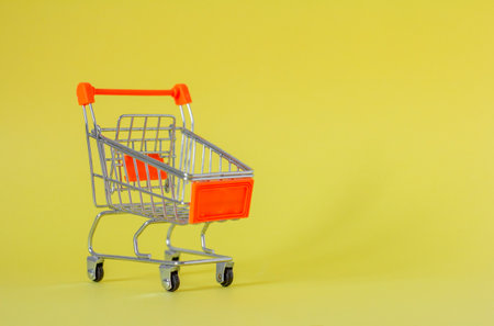 Metal shopping cart on a yellow background with a place to copy. A symbol of trade and salesの写真素材