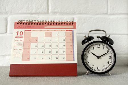 Calendar with alarm clock on white brick wall background. Time management concept.