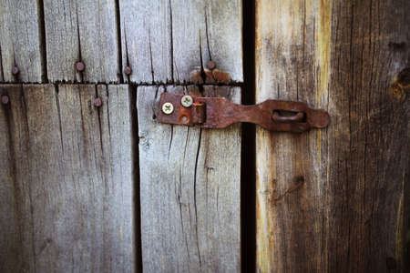 Old rusty lock hanging on the gray wooden door. Door rusty loop