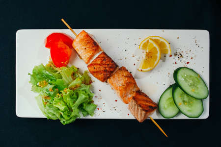 Shashlik of salmon with vegetables on white plate and black background.の写真素材