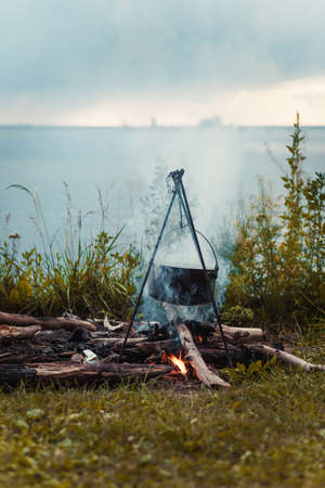 Travel a kettle over a fire burning on the river and sunset backgroun.Cooking over a campfireの写真素材
