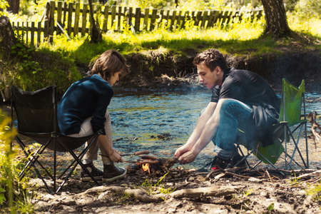 The guy with the girl sitting at the river fry sausagesの写真素材