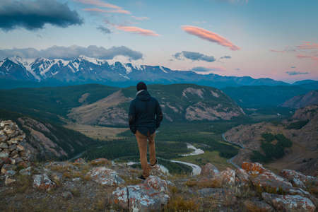 Rear view of man tourist enjoying beautiful panorama in the evening on the blurred background snow-covered mountainsの写真素材