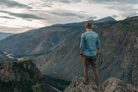 The traveler in a hat costs on the edge of the high rock and looks to the valley of a canyonの写真素材