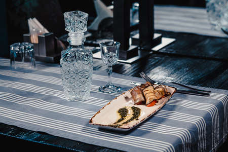 Fried eggplants stuffed with tomato and cheese on a white plate with sauce. On a blue tablecloth striped with knife and fork. Clouse up. On the table is a crystal decanter and a glassの写真素材