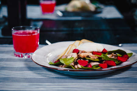 White plate with poached egg in salad with knife and fork. Next glass with red juice. Blue tablecloth on the background. Clouse upの写真素材
