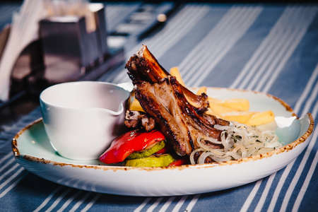 Plate with rack of lamb, grilled vegetables and french fries. Clouse up. Plate on the table with a tablecloth. In a restaurantの写真素材