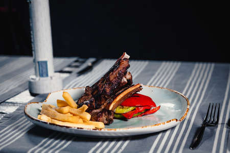 Plate with rack of lamb, grilled vegetables and french fries. Clouse up. Plate on the table with a...
