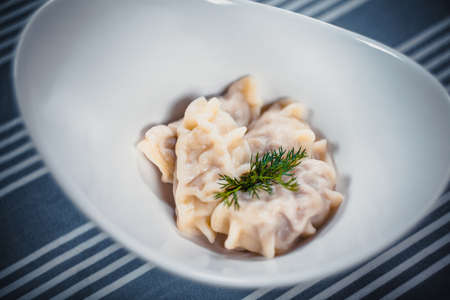 Top view of Russian dumplings in a white plate with greens. Plate on the table with a blue tablecloth in white strips. Clouse up food.の写真素材