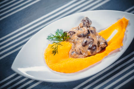Top view of chicken hearts with mashed potatoes on a white plate. Plate on the table with a blue...