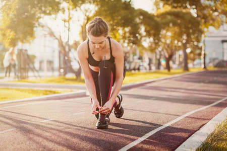 Jogging girl tie shoe laces on her sport shoes getting ready to run. Close up on sporty lady doing...