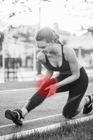 Athletic woman on running track touching hurt leg with knee injury during workout