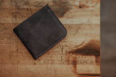 Black leather wallet on wooden background. Top view.