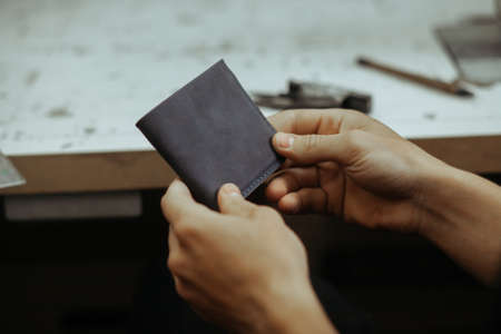 Leather goods master hands and handmade leather wallet. Workflow in the workshop. Workflow in the...