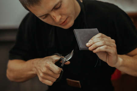 Close up of leather craftsman working with natural leather and tools. Handmade master at work in...