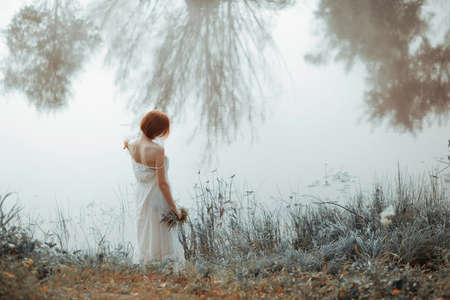 Women in white dress by river with plants in handの写真素材