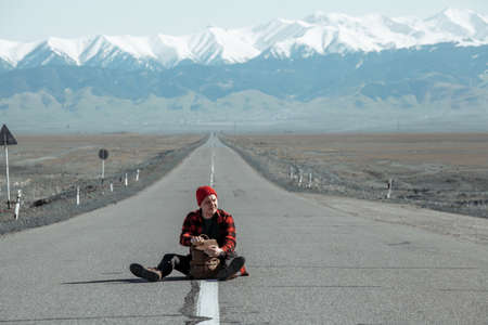 Travelling man sitting in middle of the road with backpackの写真素材
