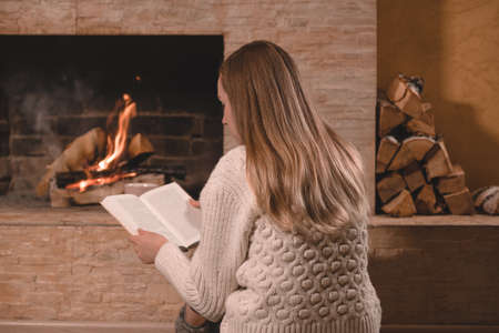 Young blond woman with book sitting near by the brick fireplaceの写真素材
