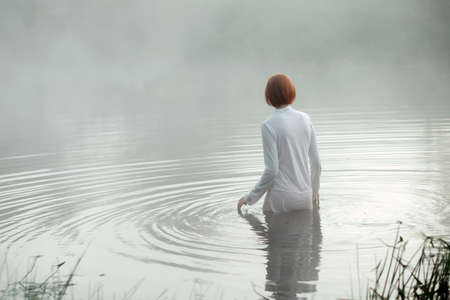 Fairy young woman standing in misty autumn lakeの写真素材