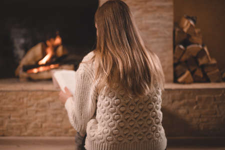 Pretty girl in sweater sitting by the fireplaceの写真素材