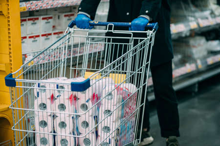 Man in protective gloves buying toilet paper in shop.
