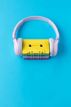 Minimalist art photography inspired by music. Yellow cassette tape on a bright blue background with rose headphones. Giant retro headphones around colorful cassette tapes.の写真素材