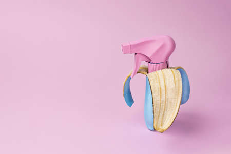 Pink sprayer in a banana skin. Rose sprinkler in a blue-colored banana peel on a pale pink background. Disinfection by using the power of nature. Creative art, minimalist art photography.の写真素材