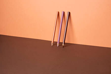 Three graphic pencils standing on a wall. Contrast brown and pastel peach background. Minimalism art photography inspired by school time. Creative layout of back to school. Season concept.の写真素材