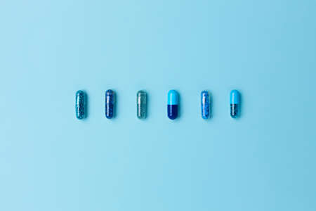 Heap of vivid blue capsule pills close up background. Creative layout of pills and capsules on blue...