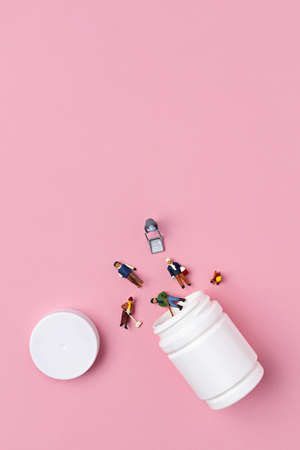 Miniature people coming out of pill box on pink background. Minimal pop art social life concept. Flat lay.の写真素材