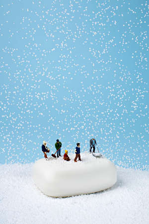 Miniature people on the white soap working on snow. Minimal winter activity concept. Flat lay.