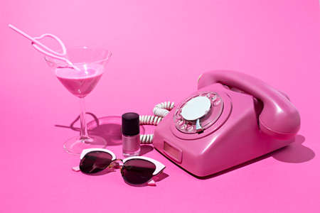 Old style rotary telephone on pink background with cocktail, sunglasses and nail polish. Minimal retro 80's concept. Flat lay.の写真素材