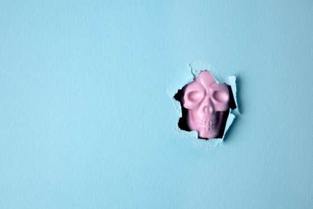 Halloween pink skull breaking through pastel blue wall. Minimal holiday celebration funny concept. Bright autumn season background.の写真素材